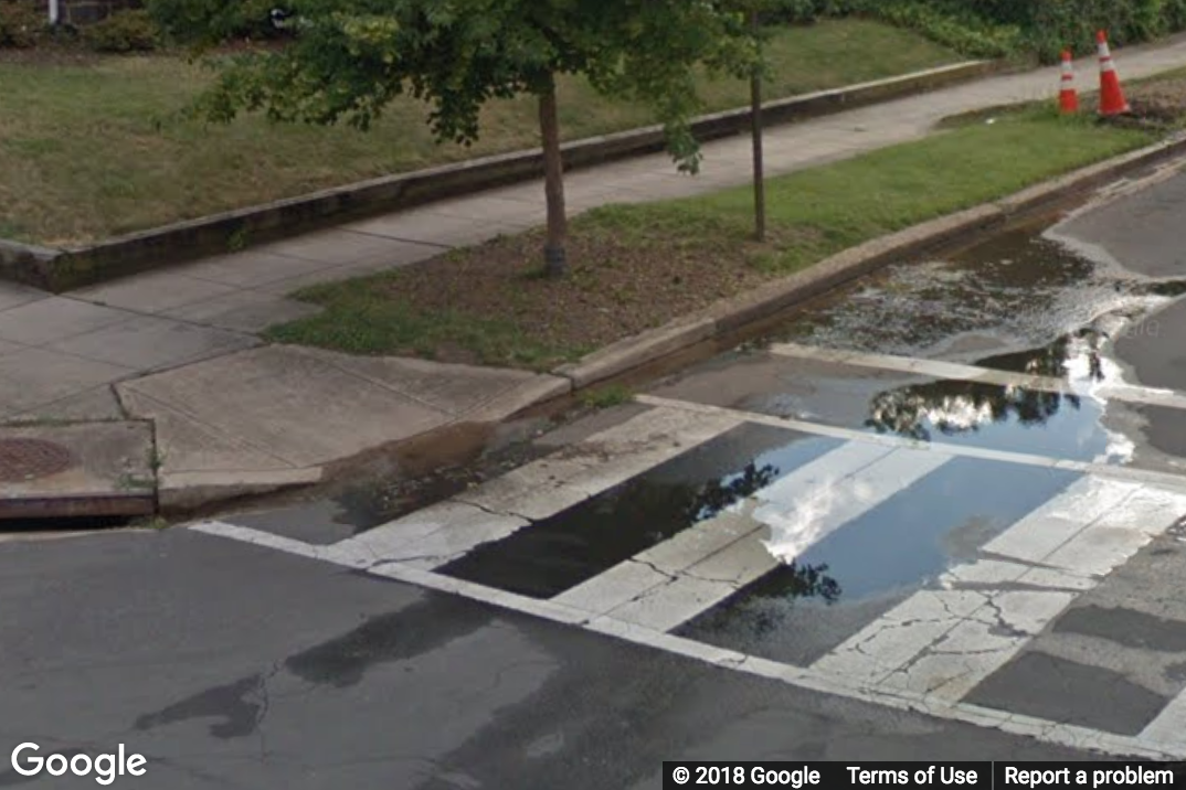 A Street View image of a curb ramp with pooled water