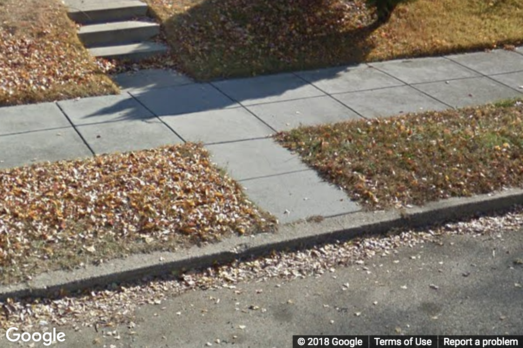 A Street View image of an extension of a walkway to a house with no curb ramp